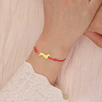 Bracelet with a gold dog charm on a red cord worn on a wrist.