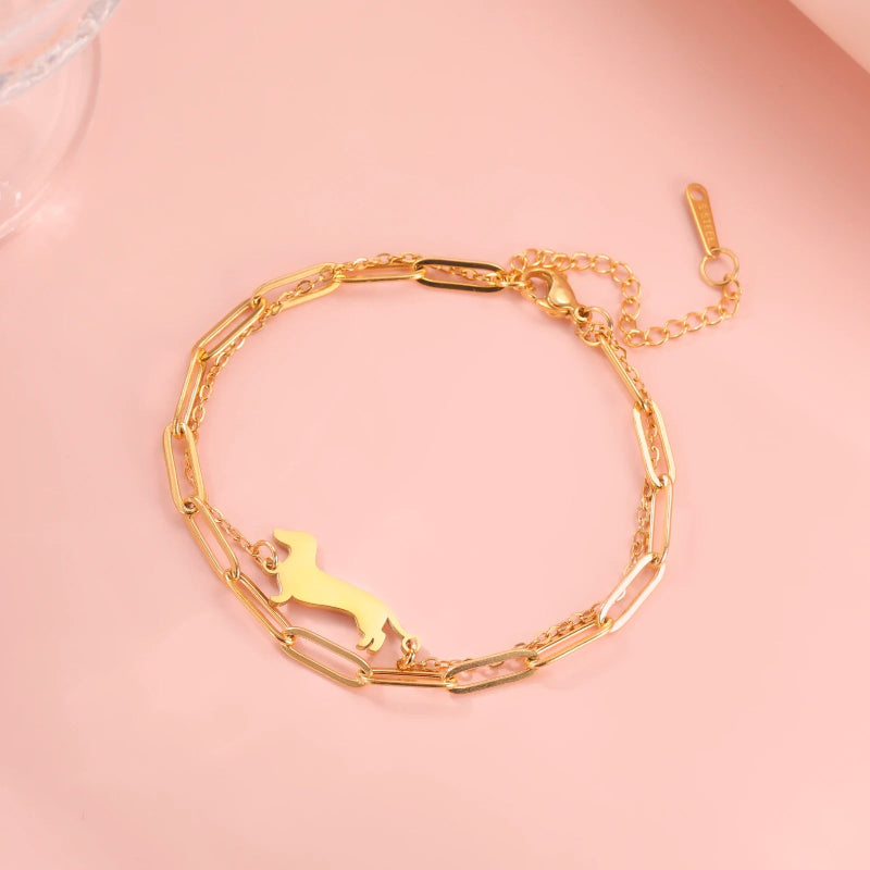 Gold bracelet with a dog-shaped charm on a pink background