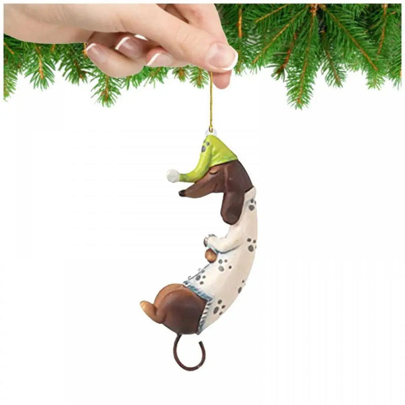 Christmas ornament of a dachshund in a green hat hanging from a hand against a white background with greenery.