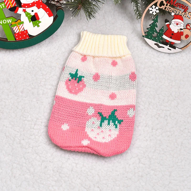 Pink and white knitted dog sweater with strawberry pattern on a light gray surface.