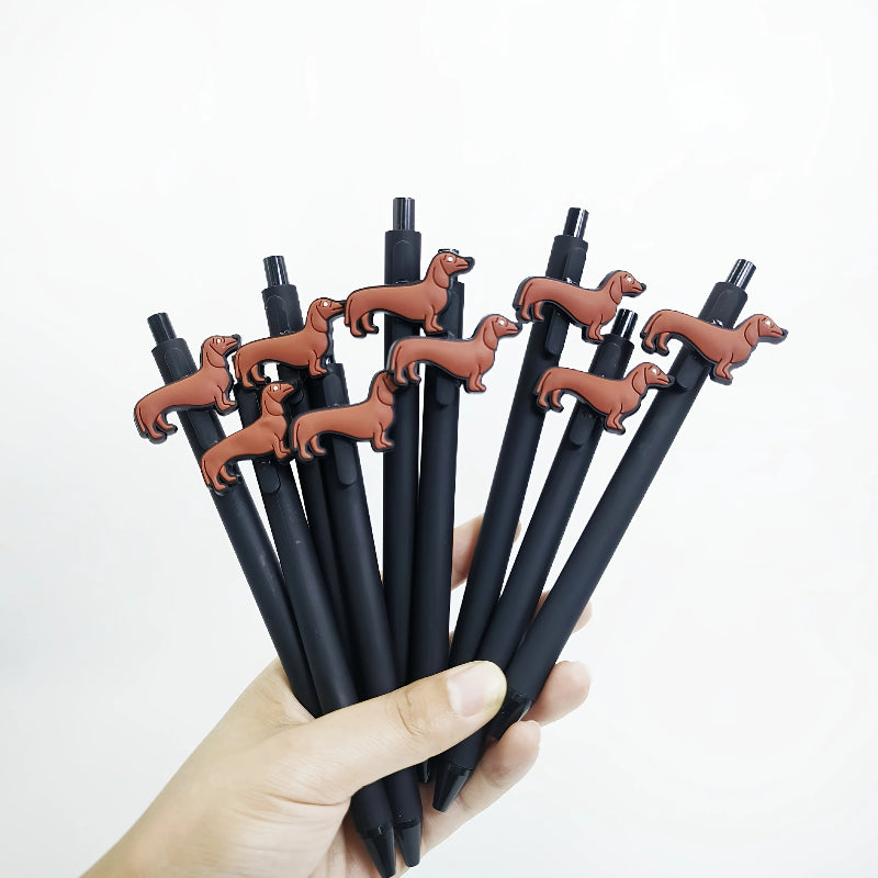 Hand holding black pens with dachshund-shaped clips against a white background